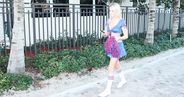 Hoy blonde cheerleader walking alone looking at her mobile handheld unit.